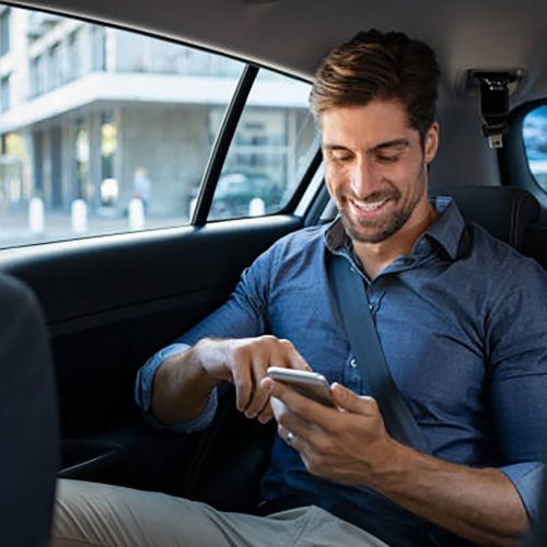 600 Happy smiling businessman man typing message on phone while sitting in a taxi. Young businessman in formal clothing using smartphone while sitting on back seat in car. Cheerful guy messaging wirth cellphone.